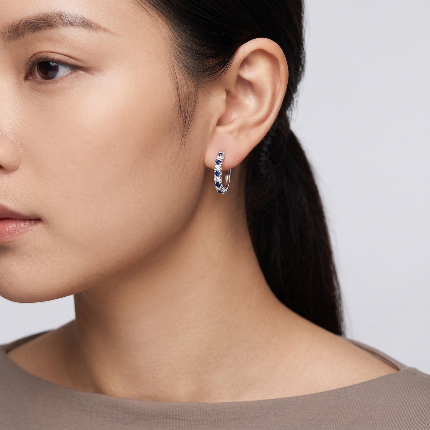 Model wearing an 18K white gold hoop earring with alternating blue sapphires and diamonds