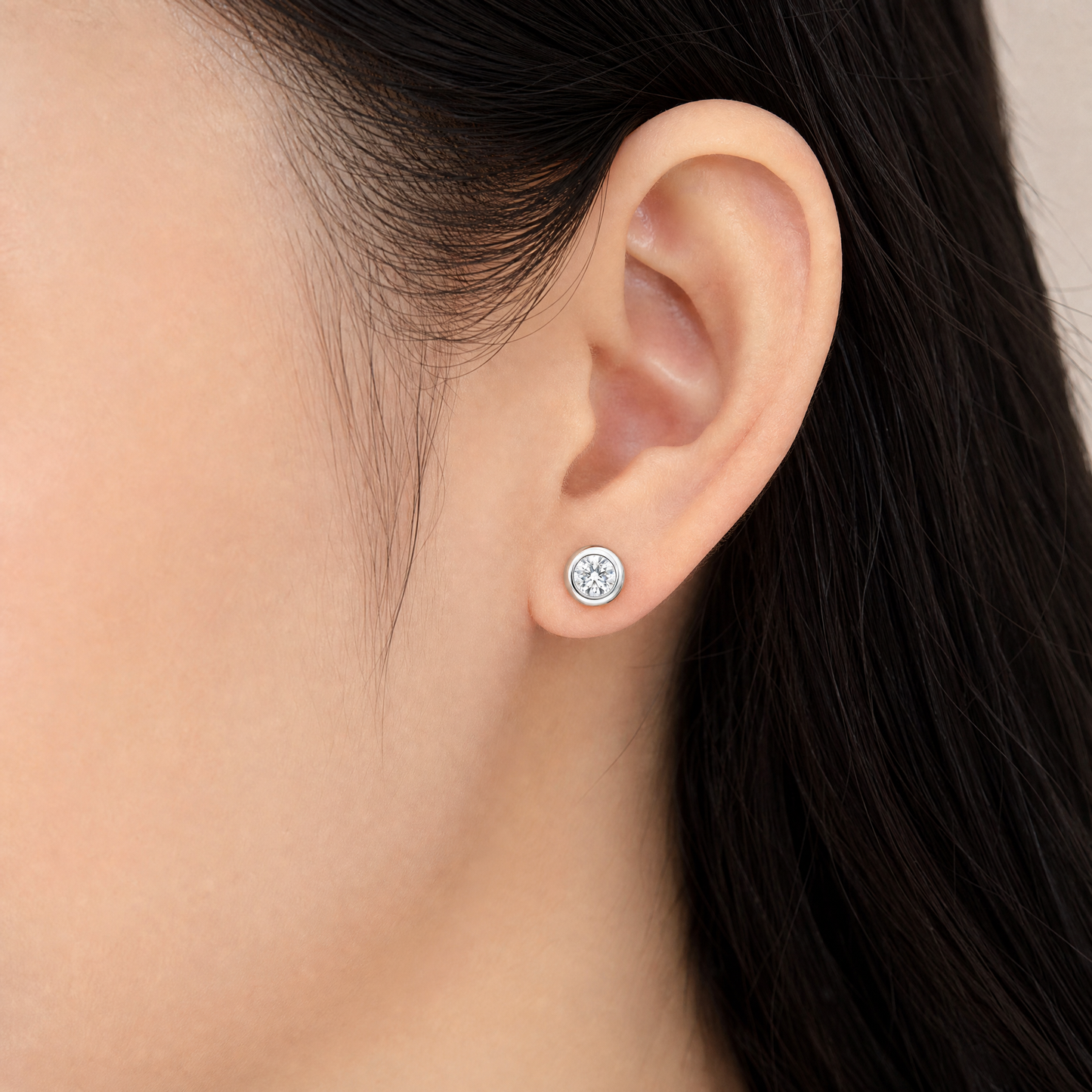 DECA0878W model shot - round brilliant diamond bezel-set white gold stud earring worn on ear