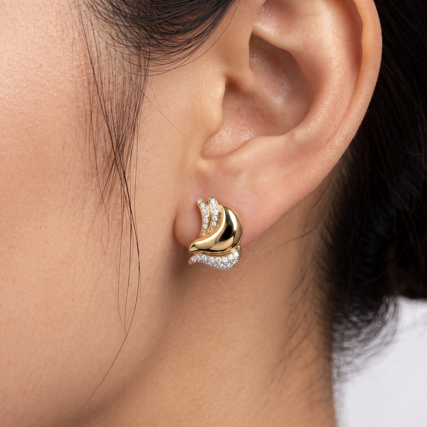 DESL0024 M-1 model shot - a model wearing the sculptural diamond swirl clip earring in 18K yellow gold, sitting flush against the earlobe, with the mirror-polished gold body and pave diamond ribbons visible