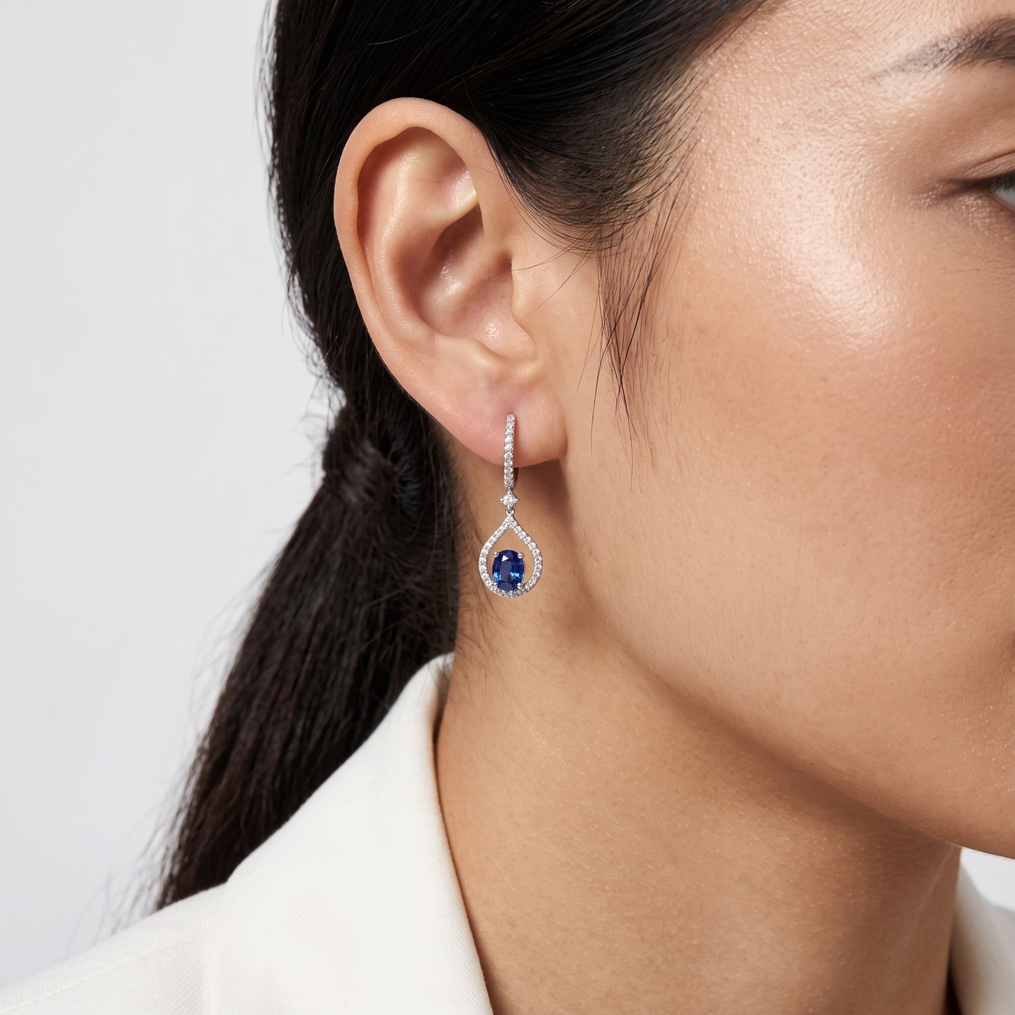 Model wearing a 14K white gold oval blue sapphire and diamond teardrop drop earring