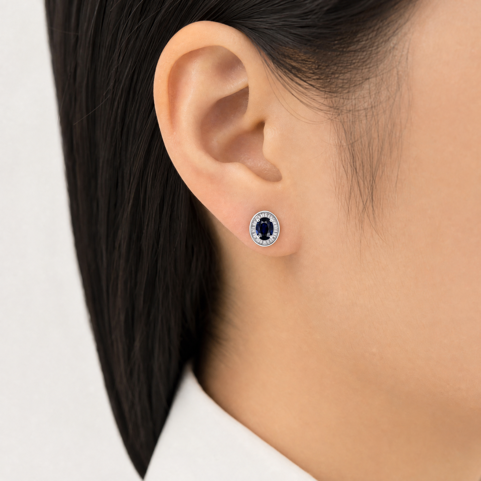 SETM0306AW model shot - oval blue sapphire tapered baguette halo stud earring worn on ear